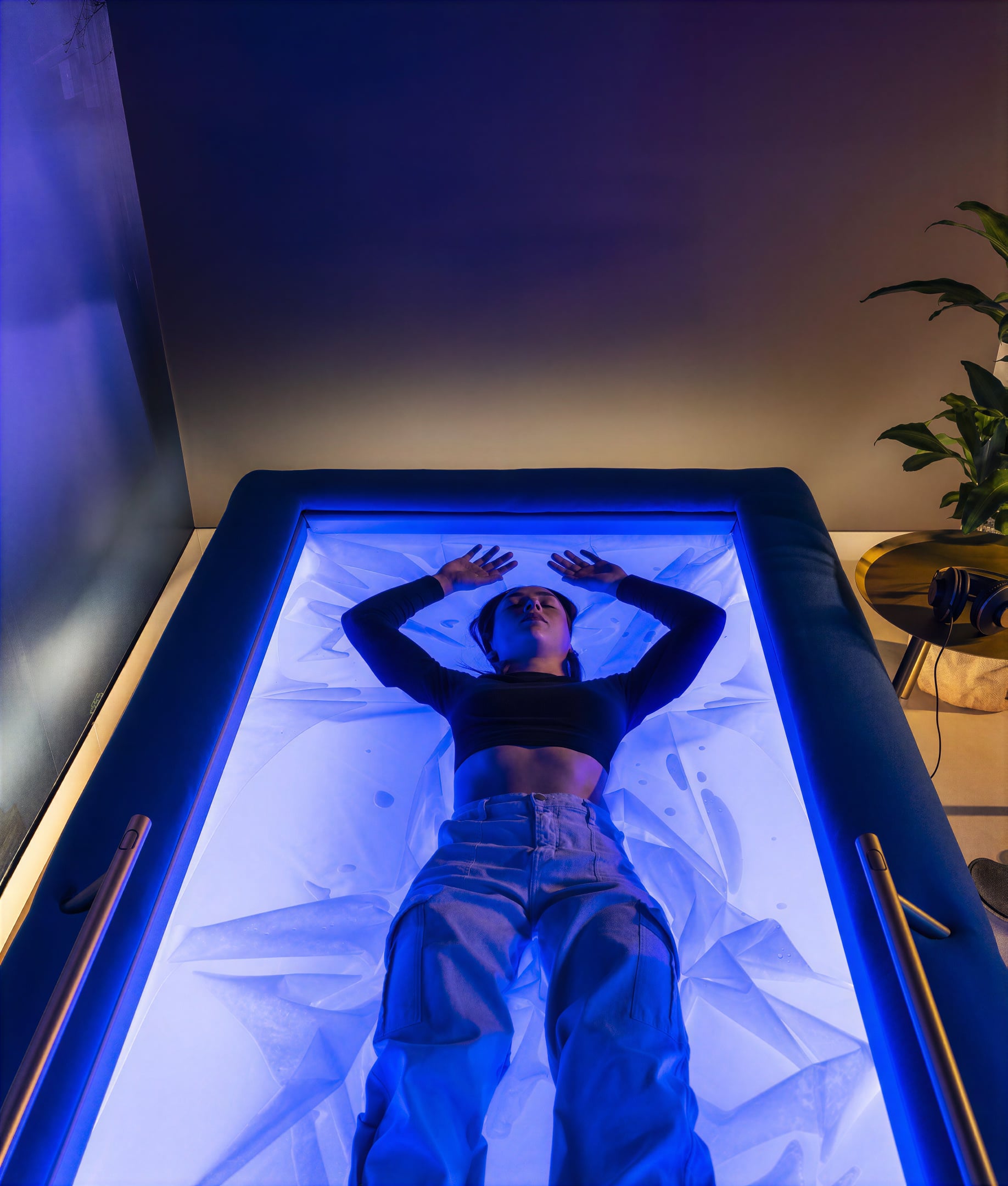 A person resting in a blue-lit floatation pod